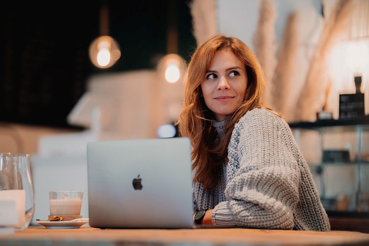 Smiling woman sitting in a cafe with her laptop open; effective rewards concept