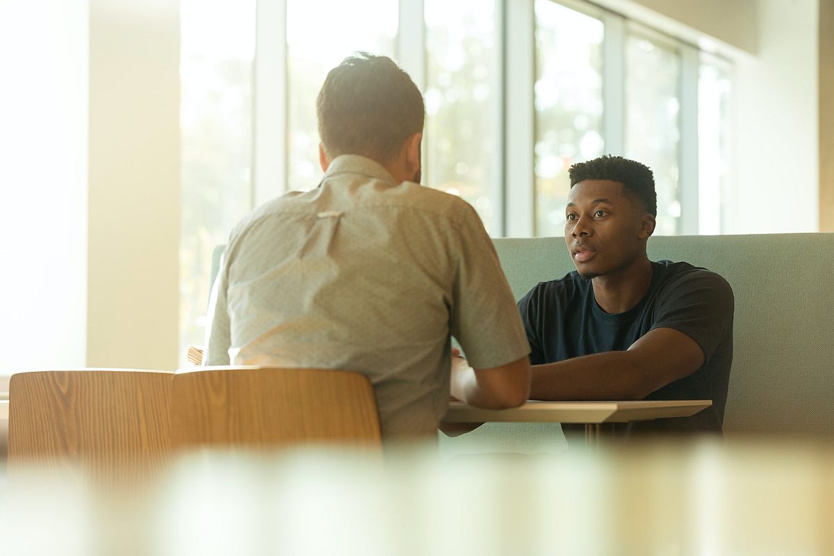 two men converse at a desk; rewards visibility concept
