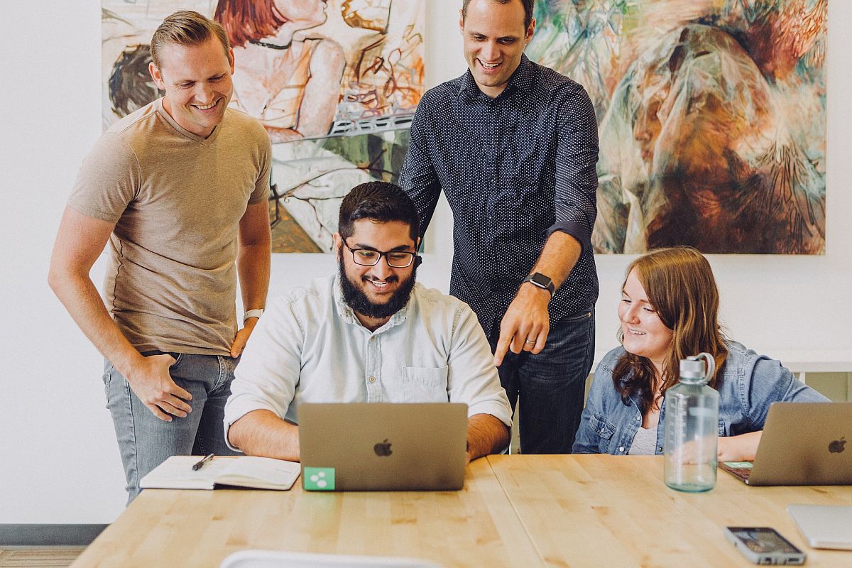 People gathered around one man at a laptop, smiling; improve employee rewards concept.