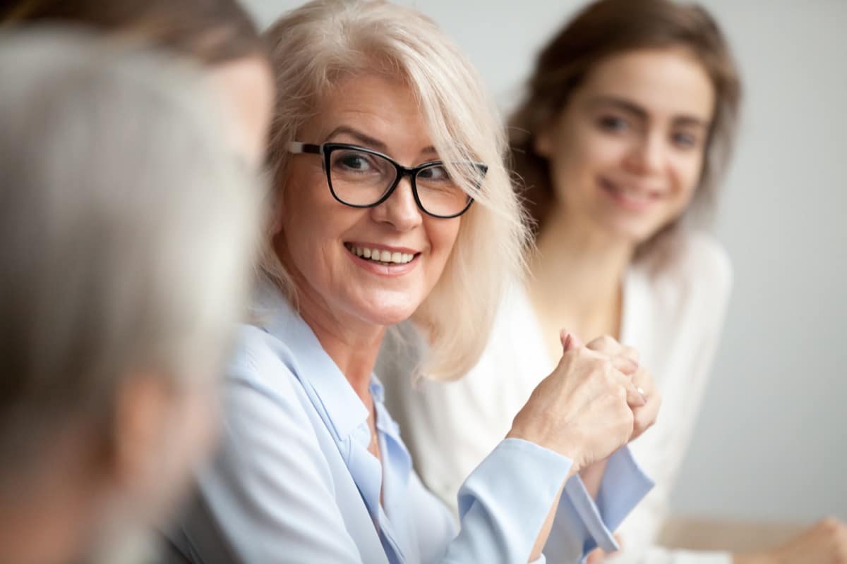 Smiling businesswoman in glasses looking at colleague at team meeting; retention strategy concept