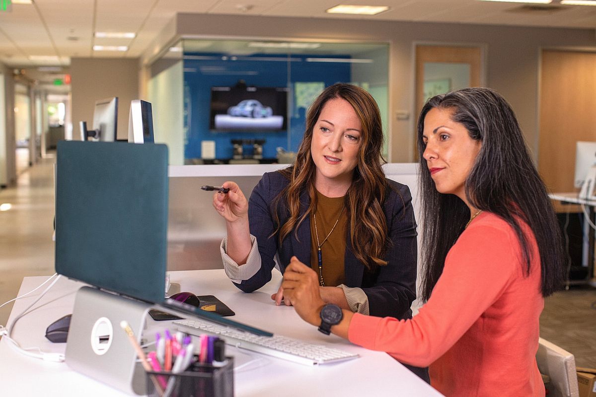 Two women talking in front of desktop computer; granular rewards data concept