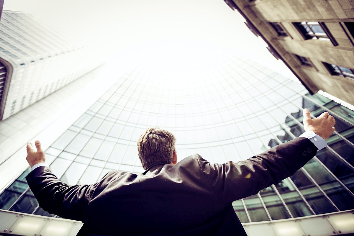 Business man lifting his arms outside, surrounded by large buildings; employee recognition concept