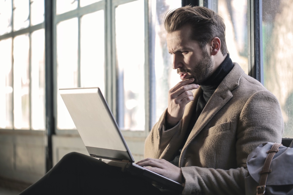 Bearded man looking pensively at laptop