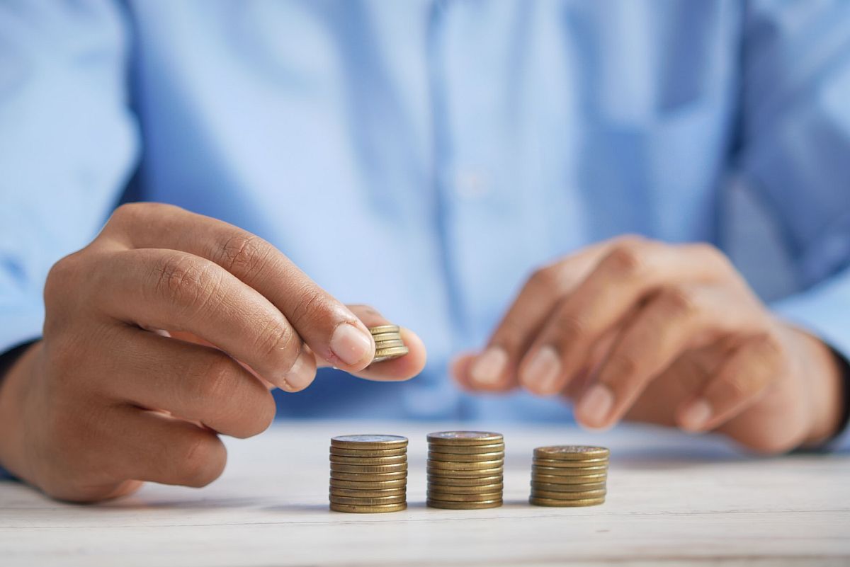 Close-up of man making even piles of coins; pay equity concept