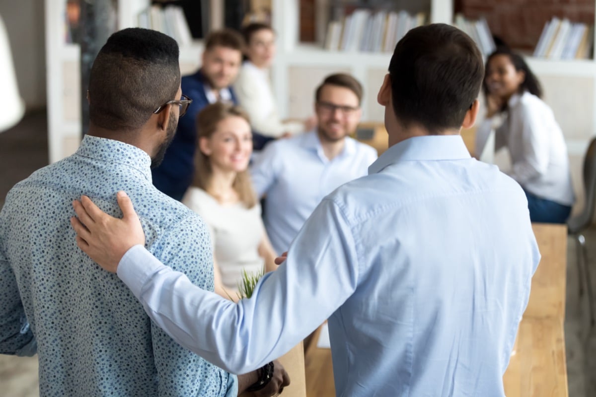 Two men standing in front of smiling colleagues; retention strategy concept