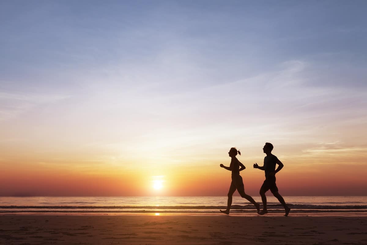 Silhouette of two runners on the beach at sunset; healthcare benefits concept