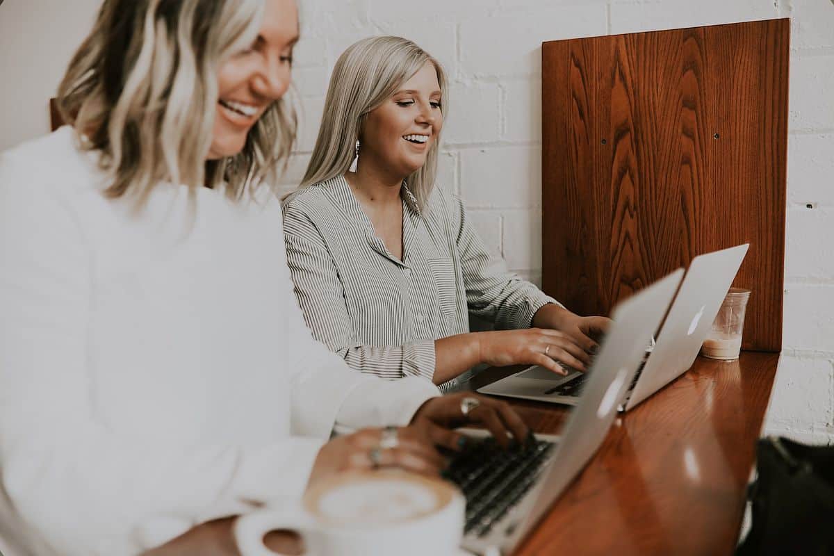 Two smiling women working on their laptops, side by side; employee trust concept