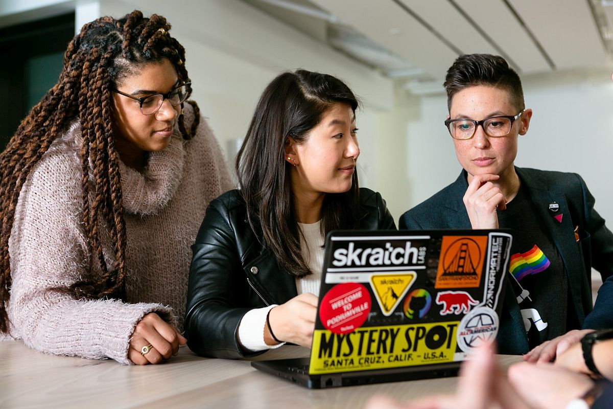 Three young people in discussion with lap top open; wage gap concept