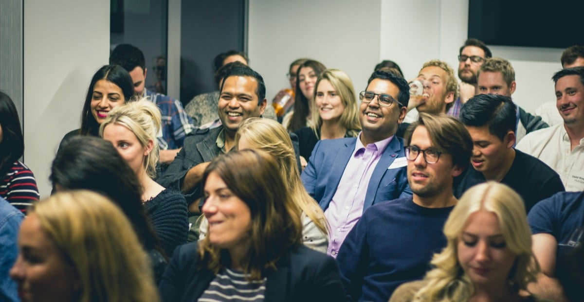 smiling faces of young professionals in a crowded conference room; hr technology conference concept