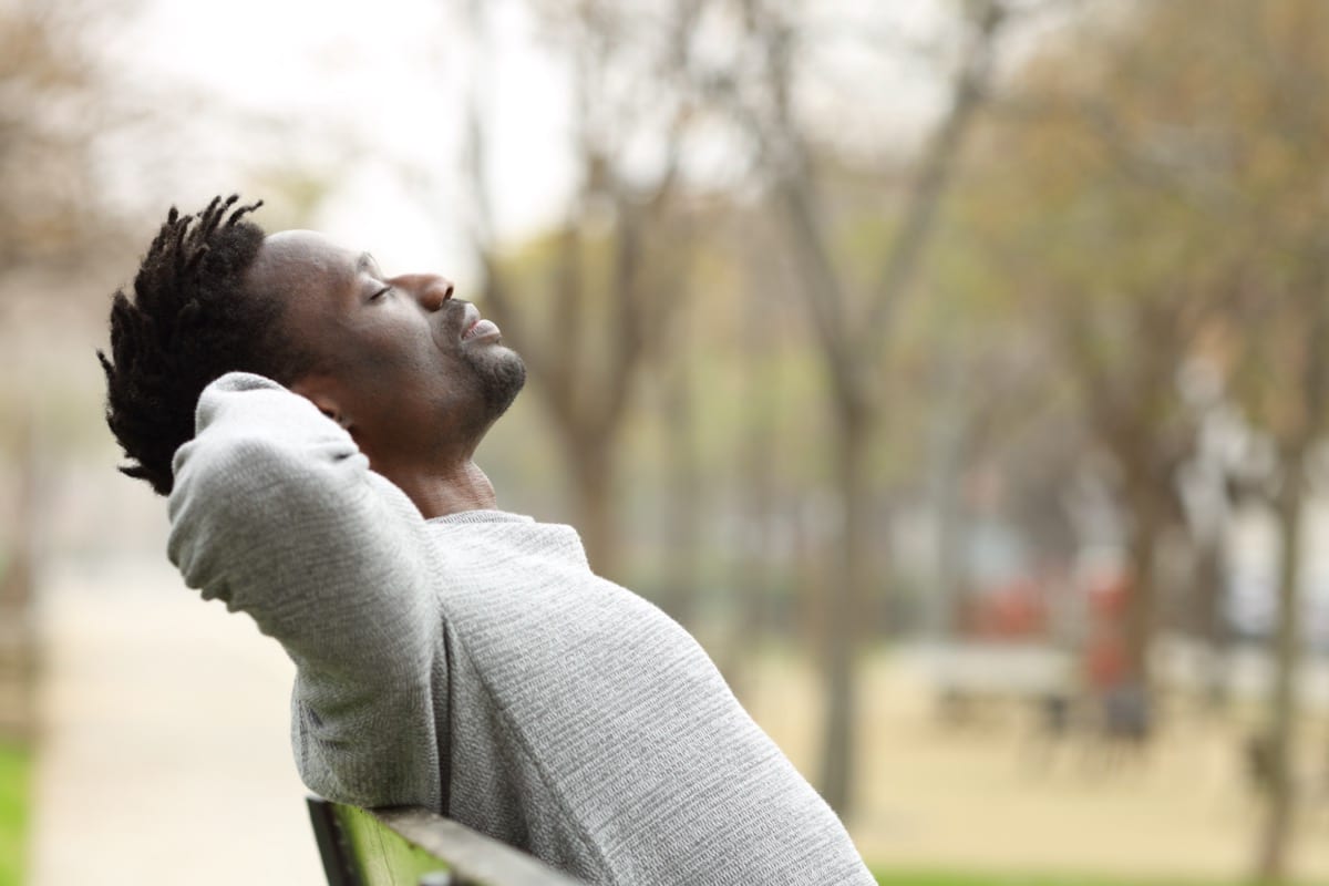 Side view portrait of a man relaxing sitting on a bench in a park; healthcare benefits concept