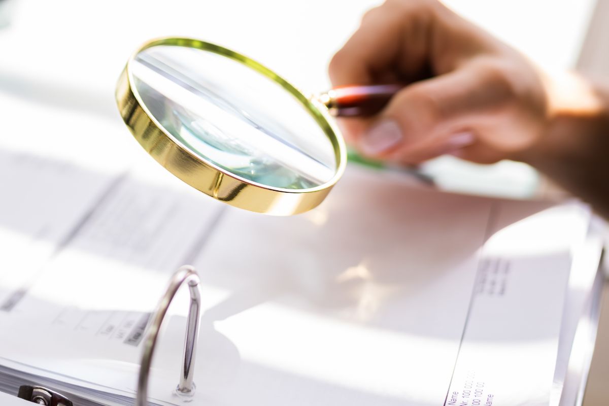 Person using a magnifying glass to look at financial paperwork
